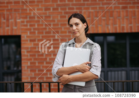 Beautiful woman in business attire standing on city street. Female university professor in front of university building. Beautiful woman in business attire standing on city street. Female university professor in front of university building. 108728390