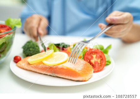 Asian elderly woman patient eating salmon steak breakfast with vegetable healthy food in hospital. Asian elderly woman patient eating salmon steak breakfast with vegetable healthy food in hospital. 108728557
