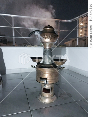 Turkish heat samovar on wood. It has a kettle. There is smoke. On the street night. 108729159