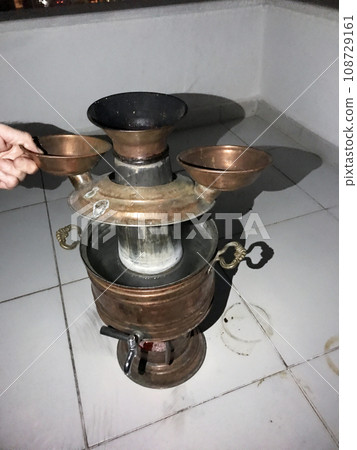 Turkish heat samovar on wood. The lid is raised, boiling water on the street is dark. Turkish heat samovar on wood. The lid is raised, boiling water on the street is dark. 108729161