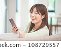 A woman who operates a smartphone in the living room 108729557