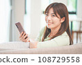 A woman who operates a smartphone in the living room 108729558