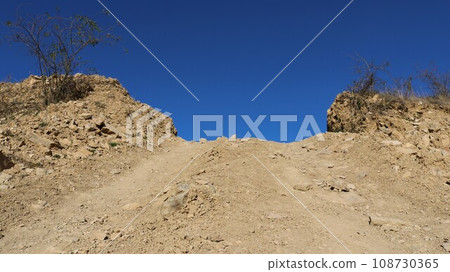 sandy path from bottom to top among limestone boulders and dry plants, a combination of white and blue natural colors in a desert landscape, a road in a lime quarry sandy path from bottom to top among limestone boulders and dry plants, a combination of white and blue natural colors in a desert landscape, a road in a lime quarry 108730365