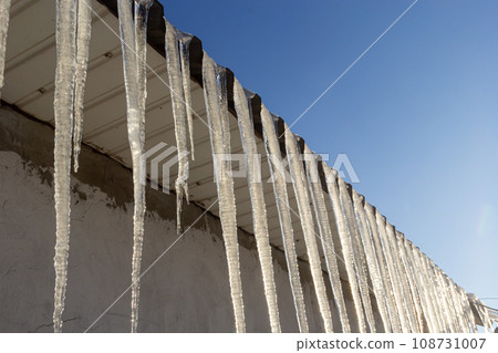 Sharp icicles and melted snow hanging from the eaves of the roof. Beautiful transparent icicles slowly gliding of a roof Sharp icicles and melted snow hanging from the eaves of the roof. Beautiful transparent icicles slowly gliding of a roof 108731007