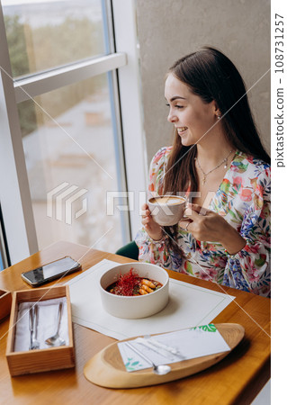 Young beautiful stylish woman drinking coffee while sitting in restaurant and eating tasty dish Young beautiful stylish woman drinking coffee while sitting in restaurant and eating tasty dish 108731257
