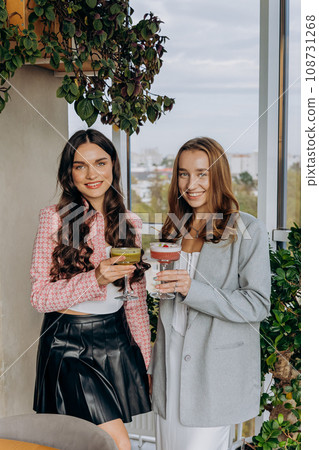 Attractive women are clinking and toasting with cocktails in restaurant or bar while looks camera 108731268