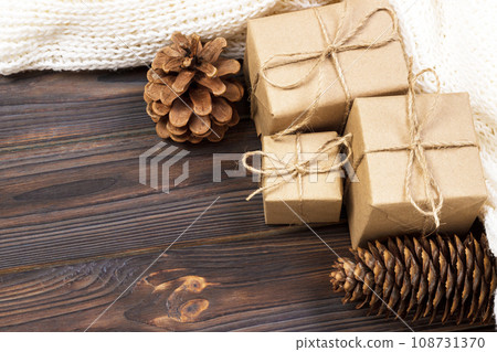 Christmas gifts and white scarf on a black wooden table with cones 108731370