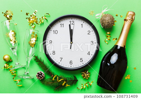 New year celebration concept with a bottle of champagne and two glasses toasting. Christmas gift box, alarm clock and fir tree branch on colored table. Top view Copy space New year celebration concept with a bottle of champagne and two glasses toasting. Christmas gift box, alarm clock and fir tree branch on colored table. Top view Copy space 108731409