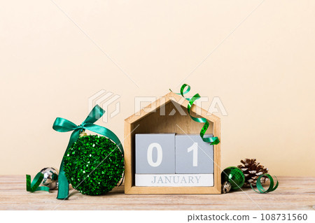 1 january. Christmas composition on colored background with a wooden calendar, with a gift box, toys, bauble copy space 1 january. Christmas composition on colored background with a wooden calendar, with a gift box, toys, bauble copy space 108731560