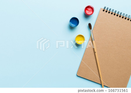 Album pages and paints, pencils, brush on a colored background. Top view with empty space. workplace for creativity. home teaching concept drawing 108731561