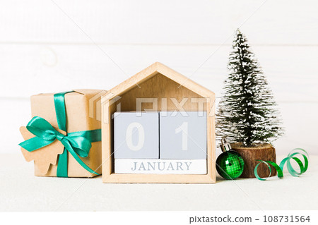 1 january. Christmas composition on colored background with a wooden calendar, with a gift box, toys, bauble copy space 108731564