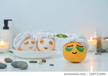 Orange fruits with towel and patches under eyes. Spa treatment and self care concept Orange fruits with towel and patches under eyes. Spa treatment and self care concept 108731890