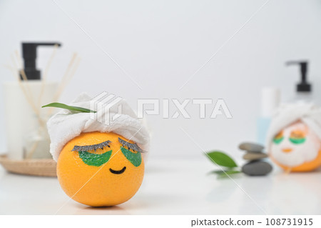 An orange fruit with towel and patches under eyes. Spa treatment and self care concept. 108731915