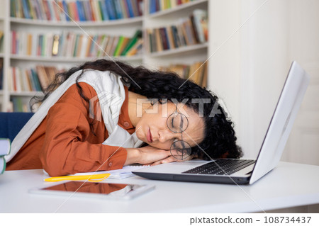 Young attractive female office worker wearing glasses fell asleep at workplace in front of laptop sitting at desk in office, overtired at work, overwork due to busy schedule. Young attractive female office worker wearing glasses fell asleep at workplace in front of laptop sitting at desk in office, overtired at work, overwork due to busy schedule. 108734437