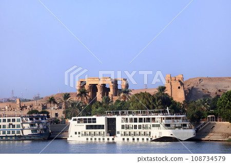 Cruise ship on Nile river near Kom Ombo Temple of gods Horus and Sobek, Egypt, Africa. Luxury Nile Cruise. Summer vacation, relaxing on cruise ship. Com-Ombo Temple in the light of sunset Cruise ship on Nile river near Kom Ombo Temple of gods Horus and Sobek, Egypt, Africa. Luxury Nile Cruise. Summer vacation, relaxing on cruise ship. Com-Ombo Temple in the light of sunset 108734579