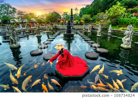 Woman feeding colorful fish in pond at Tirta Gangga Water Palace in Bali, Indonesia. 108734824