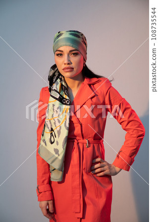a woman in a headscarf in an orange dress stands indoors 108735544