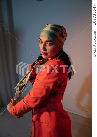 a woman in a headscarf in an orange dress stands indoors a woman in a headscarf in an orange dress stands indoors 108735547