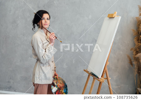 a female artist stands at an easel with a brush and is about to paint a picture 108735626