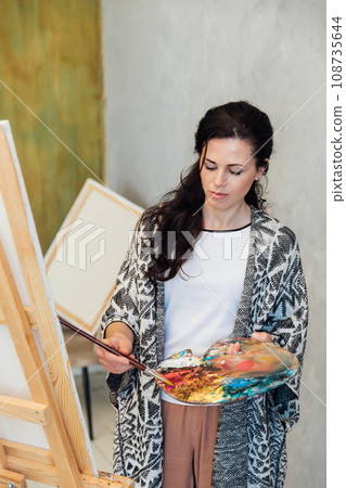 a female artist stands at an easel with a white canvas on a gray background 108735644