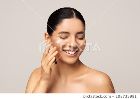 Seasonal face skin protection. Beauty shot of gorgeous multiracial woman with amazing smile applying cream on her face 108735981