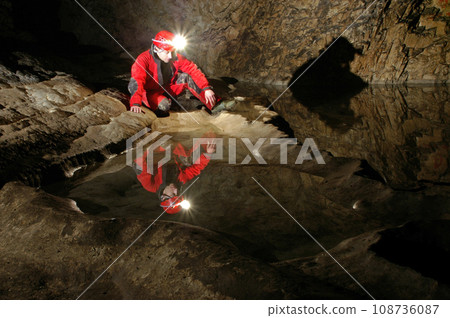 Reflection of a spelunker in a cave water pool. Acetylene gas lamp on helmet illuminating the undeground 108736087
