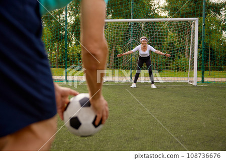 Elderly woman standing at gates getting ready to catch soccer ball 108736676