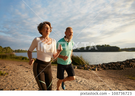 Happy elderly couple running on beach enjoying jogging workout in morning 108736723