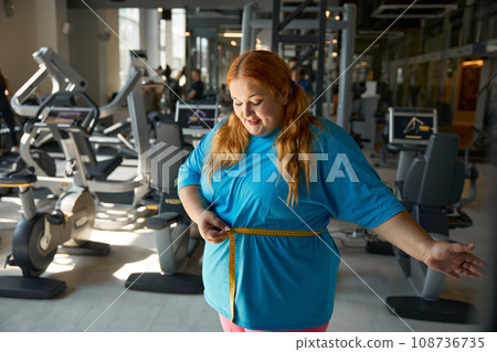 Happy satisfied overweight woman seeing good result on measuring tape Happy satisfied overweight woman seeing good result on measuring tape 108736735
