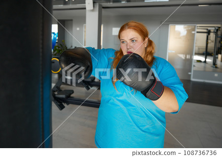 Concentrated fat woman using boxing gloves doing punching exercises 108736736