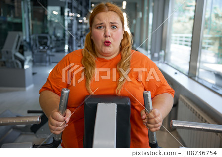 Portrait of tired obese woman working on elliptical machine Portrait of tired obese woman working on elliptical machine 108736754