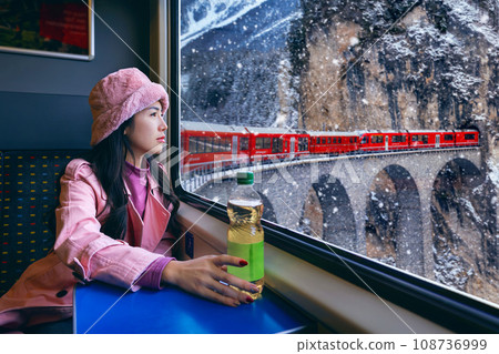 Tourist looking out the window enjoying with Train passing through famous mountain in Filisur, Switzerland. Landwasser Viaduct world heritage with train express in Swiss Alps snow winter scenery. 108736999