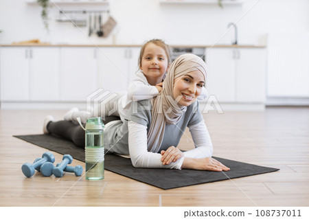 Muslim female in hijab relaxing with cute daughter after fitness routine at home Muslim female in hijab relaxing with cute daughter after fitness routine at home 108737011