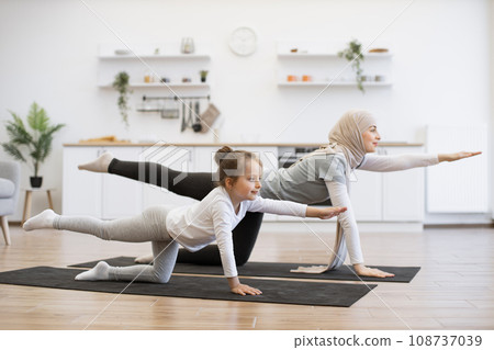 Beautiful mother with her girl practicing yoga exercise together in kitchen. Beautiful mother with her girl practicing yoga exercise together in kitchen. 108737039