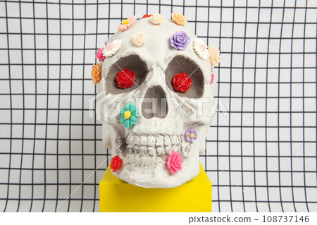 a skull covered with multiple plastic flowers on a white squared tile pattern a skull covered with multiple plastic flowers on a white squared tile pattern 108737146