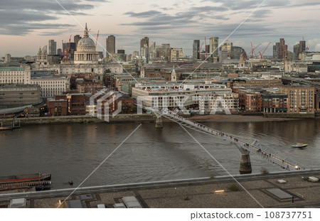 High angle view St Paul Cathedral and The skyscrapers with Thames river and Millennium Bridge on foreground at sunset. High angle view St Paul Cathedral and The skyscrapers with Thames river and Millennium Bridge on foreground at sunset. 108737751