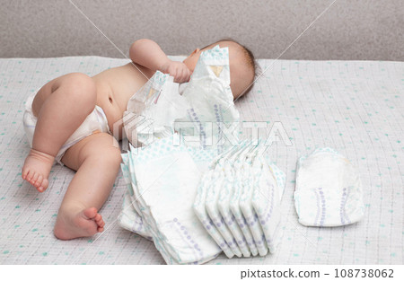 A little caucasian baby boy in a diaper lies on a white background and plays with a bunch of diapers. Copy space for text A little caucasian baby boy in a diaper lies on a white background and plays with a bunch of diapers. Copy space for text 108738062