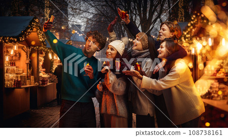 Cozy winter fair. Young happy people, friends taking selfie together, drinking mulled wine, celebrating holidays outdoors 108738161
