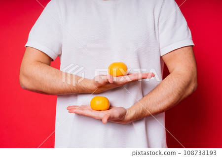 Young handsome man with dark hair with tangerine in shirt on red background 108738193