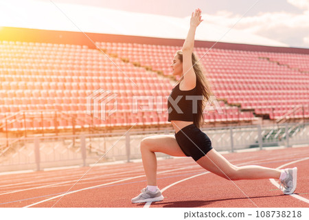 A female coach with dark hair stands on the red running track of the stadium A female coach with dark hair stands on the red running track of the stadium 108738218