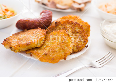 Fried grated potato pancakes with fried sausage on white plate 108738362