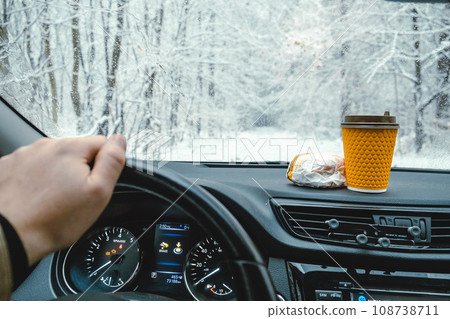 The steering wheel of a car, a hamburger and coffee on the dashboard, a winter road The steering wheel of a car, a hamburger and coffee on the dashboard, a winter road 108738711