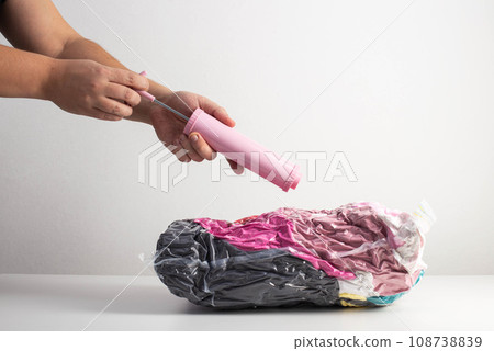 Man's hands pump air out of a sealed bag with a hand pump. Vacuum bags for storing things and clothes. Copy space for text Man's hands pump air out of a sealed bag with a hand pump. Vacuum bags for storing things and clothes. Copy space for text 108738839