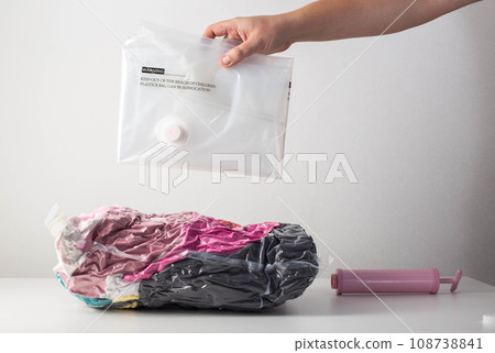 A man's hand holds vacuum bags for storing clothes and things on a white background. Pumping air out of bags with a hand pump, close-up A man's hand holds vacuum bags for storing clothes and things on a white background. Pumping air out of bags with a hand pump, close-up 108738841