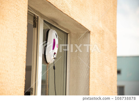 A modern vacuum robot window washer washes glass in an apartment on a balcony. View outside from the street. Safety from falls from a height. 108738878