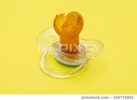 Low-quality torn baby silicone pacifier on a yellow background, close-up. Concept of the anatomical shape of the pacifier, teething in children. Low-quality torn baby silicone pacifier on a yellow background, close-up. Concept of the anatomical shape of the pacifier, teething in children. 108738892
