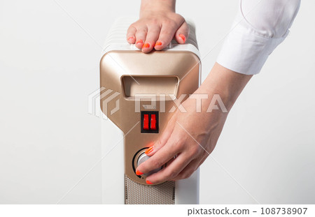 A woman's hand regulates the heating temperature on an electric heater, close-up A woman's hand regulates the heating temperature on an electric heater, close-up 108738907