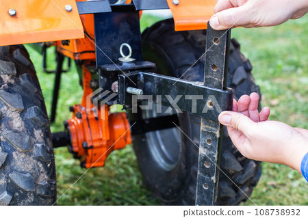 Adjustment of the coupling and attachments in a multifunctional motor cultivator for cottages. Close-up Adjustment of the coupling and attachments in a multifunctional motor cultivator for cottages. Close-up 108738932