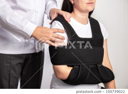 A doctor surgeon examines a girl's shoulder after surgery. Bandage on the shoulder joint during rehabilitation after surgery on the shoulder joint, tear of the shoulder cuff. Acromioclavicular joint A doctor surgeon examines a girl's shoulder after surgery. Bandage on the shoulder joint during rehabilitation after surgery on the shoulder joint, tear of the shoulder cuff. Acromioclavicular joint 108739022
