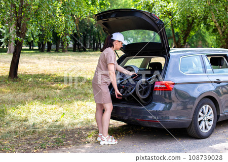 The caucasian girl puts the baby stroller in the trunk of the car. The concept of a spacious trunk in a family car. 108739028
